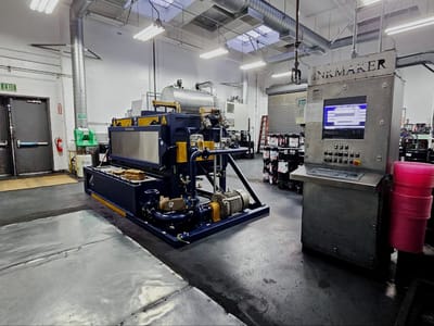 Shop machining and forming cell with its control console and guarding, set on a matted floor with stock and tooling racked along the wall.