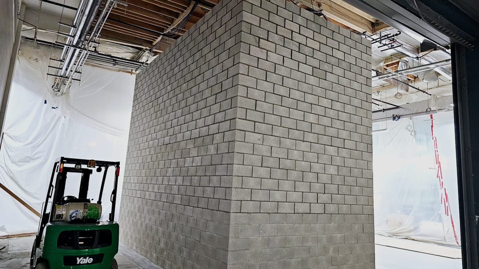 The same enclosure with the block walls laid out to full height and the opening closed, a forklift parked at the corner for scale.