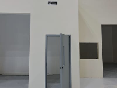Completed priming room exterior inside a plant, a smooth-finished enclosure wall with a flush personnel door standing open onto the sealed floor.