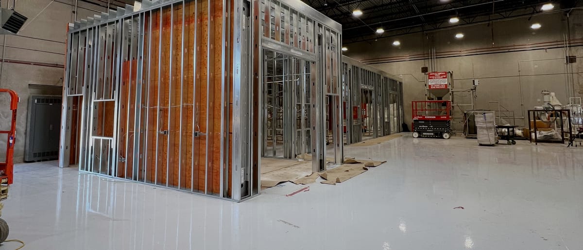 Priming room enclosure framed out inside a warehouse bay, timber and steel studs standing under exposed bar joists and roof skylights.